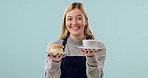 Waitress, face and woman with tea and dessert order for customer service with hospitality in studio. Coffee shop, cafe or small business employee with smile from order with cake and blue background