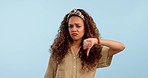 Sad, face and woman with thumbs down in studio for fail, mistake or wrong choice on blue background. Portrait, frown and female model with emoji, vote or bad reviews, feedback and rejection decision