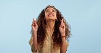 Happy, woman and fingers crossed in studio with hope for lottery, opportunity or prize giveaway on blue background. Excited, news and lady model with emoji hand sign for competition, feedback or luck