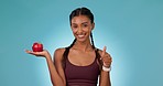 Woman, athlete and apple in hands with thumbs up, yes and  healthy decision for nutrition, wellness and benefits in diet. Happy, nutritionist and choice of fruits or food on blue background in studio