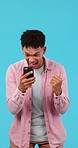 Phone, celebration and man in studio with fist pump for winning, success or achievement. Happy, excited and young male winner cheering for online bet victory on cellphone isolated by blue background.