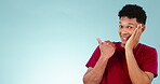 Smile, space and a man pointing to secret news on a blue background in studio for information or gossip. Portrait, mockup for advertising and a happy young person showing a marketing announcement