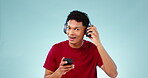 Face, listening and man with headphones, dancing and streaming music on a blue studio background. Portrait, person or happy model with headset, hearing or audio with smartphone, digital app or energy