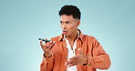 Phone call, man and angry on speaker with communication in studio for networking, audio and talk on blue background. Smartphone, person and conversation with serious face for discussion and opinion