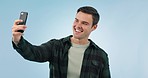 Smile, selfie and man in studio for social media, profile picture or memory on blue background. Smartphone, app and happy guy photographer influencer with photo for blog, podcast or vlog website post