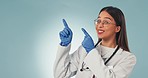 Medic, woman and point in studio, smile and decision for vote, review or advice by blue background. Happy nurse, doctor and ppe gloves for safety in mockup space, opinion and feedback with promotion