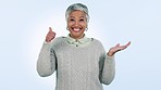 Face, senior woman and thumbs up for hand holding, pointing and support in studio on blue background. Happy, portrait and elderly female model show review, feedback or emoji success vote and approval