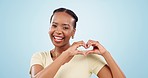 Heart, hands and face of black woman in studio for kindness, care and charity donation on blue background. Happy portrait, model and laugh for love, hope and thanks for support, emoji sign and peace