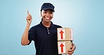 Happy black woman, box and pointing up for delivery, logistics or order against a blue studio background. Portrait of African female person or courier lady showing deal in advertising with packages
