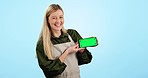 Happy woman, phone and green screen for advertising or marketing against a blue studio background. Portrait of female person or waitress smile and showing mobile smartphone app, display or mockup