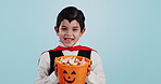 Halloween, basket and portrait of child with sweets or candy isolated in a studio blue background and happy. Holiday, laughing and kid in vampire costume for celebration in fantasy festival of horror