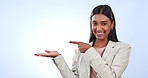 Portrait, woman is pointing at advertising and business presentation with information or news on blue background. Corporate marketing, mockup space and company launch with announcement in a studio