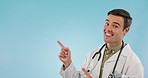 Face, pointing and doctor with a smile, man and healthcare on a blue studio background. Portrait, person and model with hand gesture, info and mockup space with medical professional and opportunity