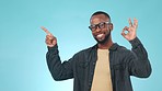 Pointing, mockup and face of black man in a studio to empty space for marketing or advertising. Happy, smile and portrait of African male model with an ok hand gesture isolated by blue background.