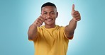 Face, smile and man with thumbs up, agreement and feedback with support on a blue studio background. Portrait, person and model with hand gesture, review and emoji with like, winning and promotion