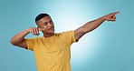 Pointing, smile and young man in studio with mockup space for marketing, advertising or promotion. Happy, casual fashion and male model from Mexico with show hand gesture isolated by blue background.