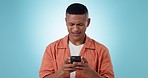 Phone, typing and young man in studio networking on social media, mobile app or the internet. Technology, moody and male model from Mexico scroll on website with cellphone isolated by blue background