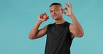 Apple, health and okay with face of man in studio for nutrition, diet and wellness. Fitness, food and detox with portrait of person and fruit on blue background for eating, fiber and organic snack