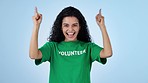 Volunteer, pointing up and face of woman on blue background for charity, donation and support. Happy, excited and portrait of person with hand gesture for volunteering, NGO project or help in studio
