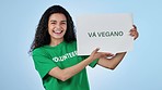 Volunteer woman, vegan poster and studio for smile on face, search and point by blue background. Recruitment, choice and call to action for sustainable food, diet and eco friendly diet in Barcelona
