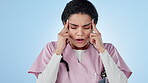 Nurse, headache and stress with woman in healthcare, breathing through pain with medical condition in studio. Health, migraine and burnout with frustrated caregiver massage temple on blue background
