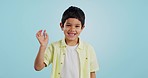 Kid, hand and waving with smile in studio on blue background in mockup with excitement. Youth, boy and greeting while looking at screen with face for announcement of offer on social media, web or app