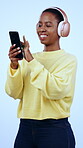 Black woman, headphones or phone for music search, social media or internet browsing on studio blue background. Laughing, mobile and technology for listening to radio, podcast and streaming selection