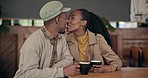 Couple, coffee and kiss with love at cafe, restaurant or diner for bond, care and romance. Black people, man and woman with tea on a weekend for break, conversation and talking for romance or date