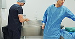 Team, doctors and washing hands, put on theatre gown or prepare to start surgery or operation in hospital. Surgeon cleaning with water, medical healthcare or nurse help man wipe for hygiene or safety