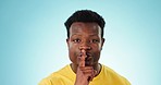 Black man, face and secret for gossip, whisper or privacy with finger on lips isolated on a blue background. Portrait of African male person, quiet and silence gesture or emoji for confidential news