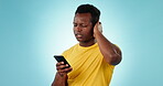 Phone, confused and anxiety with an annoyed black man in studio on a blue background for communication. Mobile, stress and worry with the reaction of a young person reading a bad news text message