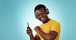 Happy black man, headphones and dancing to music with phone against a studio or blue background. African male person smile and enjoying audio streaming on mobile smartphone or sound app on mockup