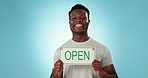 Happy black man, open sign and advertising in welcome or ready for service against a blue background. Portrait of African male person or store owner smile showing billboard for marketing on mockup