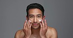 Face, man and apply of moisturiser in studio on gray background for beauty, skincare or glow in mockup. Asian, model and smile for product, sunscreen or protection by hand, hydration or anti aging