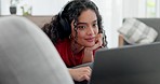 Happy woman lying on sofa with laptop, headphones and smile on social media, video streaming chat or movie. Relax, internet and happy girl on couch on computer with earphones, audio or typing on app.