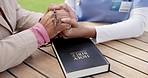 People, together and holding hands in prayer with bible for support in spiritual guidance, faith and belief. Doctor, patient and rosary for worship of religion for health, wellness or care in garden