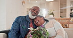 Sofa, flowers and love with a senior black couple in their home living room for anniversary celebration. Birthday, valentines day and an elderly husband hugging his wife while laughing for romance