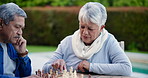 Chess, strategy and senior couple thinking while playing a board game in the garden of their home together. Mind, relax or challenge with an elderly man and woman in the backyard for problem solving