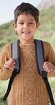 Happy, face and boy on a hike with backpack in nature on a mountain for outdoor travel holiday. Smile, excited and portrait of child or kid on an adventure, vacation or weekend trip in countryside.