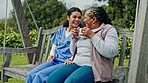 Happy woman, nurse and patient on park bench or swing in relax with coffee for healthcare in nature. Female person or medical caregiver sitting outdoor with senior, tea or beverage in care or support