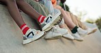 Shoes, legs and friends on rooftop in city sitting together for bonding or relax at outdoor park. Fashion, sneakers and feet with streetwear style and kick on building edge with freedom in urban town