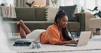 Laptop, typing and woman laying on the floor in the living room of modern apartment. Technology, elearning and young African female university student studying on a computer in the lounge at home.