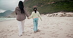 Back, beach and a mother holding hands with her daughter while walking outdoor on sand by the coast. Family, children and people on holiday or vacation together during summer for travel and bonding