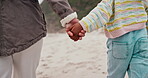 Back, beach and a parent holding hands with a child while walking outdoor on sand by the coast. Family, kids and people on holiday or vacation together during summer for travel and bonding closeup