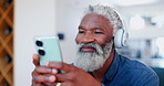 Senior man, smartphone and happy with headphones for online music, subscription and stream movie in home. African person, smile and pensioner with technology for social media, listen songs in house