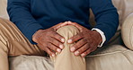 Hands, massage and man with knee pain on sofa in home or injury from accident in living room. African, person and physical therapy for ache, sore or healthcare for osteoporosis in legs or joint