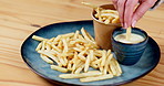 Person, hand and fast food dipping french fries on plate at restaurant for chips, potato or dish with sauce. Salted carbs for meal, snack or fresh crispy cut cuisine with dip on table for dining