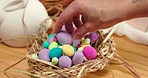 Easter, hand and decoration with egg for holiday, festive or event for celebration in home by closeup. Woman, finger and place in basket, preparation or tradition for symbol of spring, hope or faith