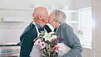 Love, surprise and senior couple with flower, gift or kiss in celebration of anniversary in a kitchen. Floral, present and romantic elderly male with bouquet for old woman in a house with support