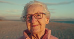 Senior woman, face and vacation by ocean, smile and freedom by beach or relaxing on holiday. Elderly person, glasses and happy in portrait or confident in retirement, nature and traveling in outdoors